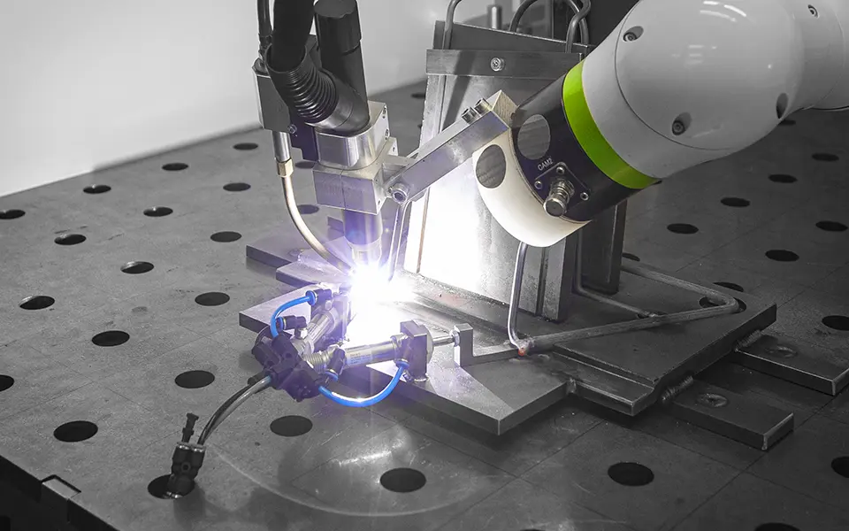 Schweißroboter verbindet Metallteile auf einem Arbeitstisch mit Spannvorrichtung.